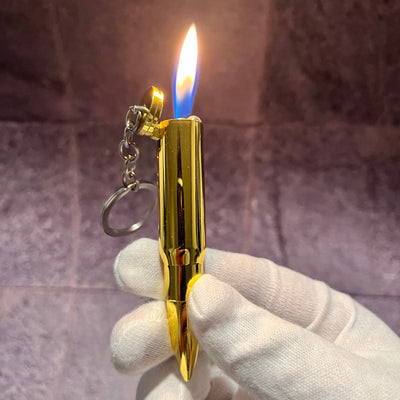 Bullet Flame Lighter – gold refillable butane lighter shaped like a bullet with flip-top cap, producing a bright soft flame while held in a gloved hand.
