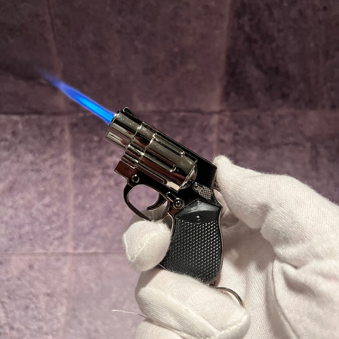 Mini Revolver Torch Lighter – refillable butane gun-shaped lighter with blue torch flame, held in a white glove