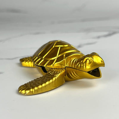 Sea Turtle Lighter – close-up of gold refillable butane lighter with detailed turtle design, displayed on white marble surface